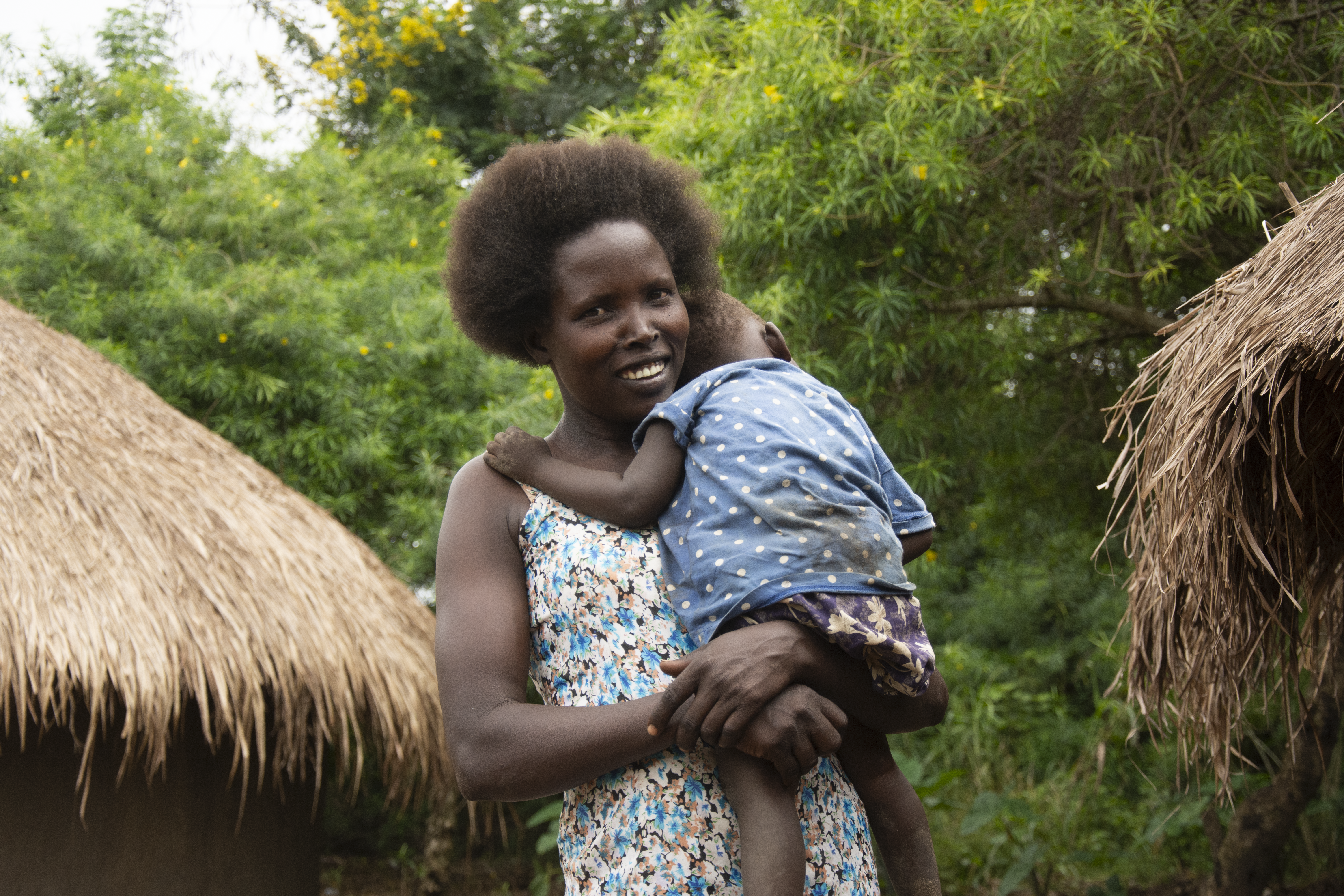 A woman stands with a baby resting on her shoulder. She is smiling