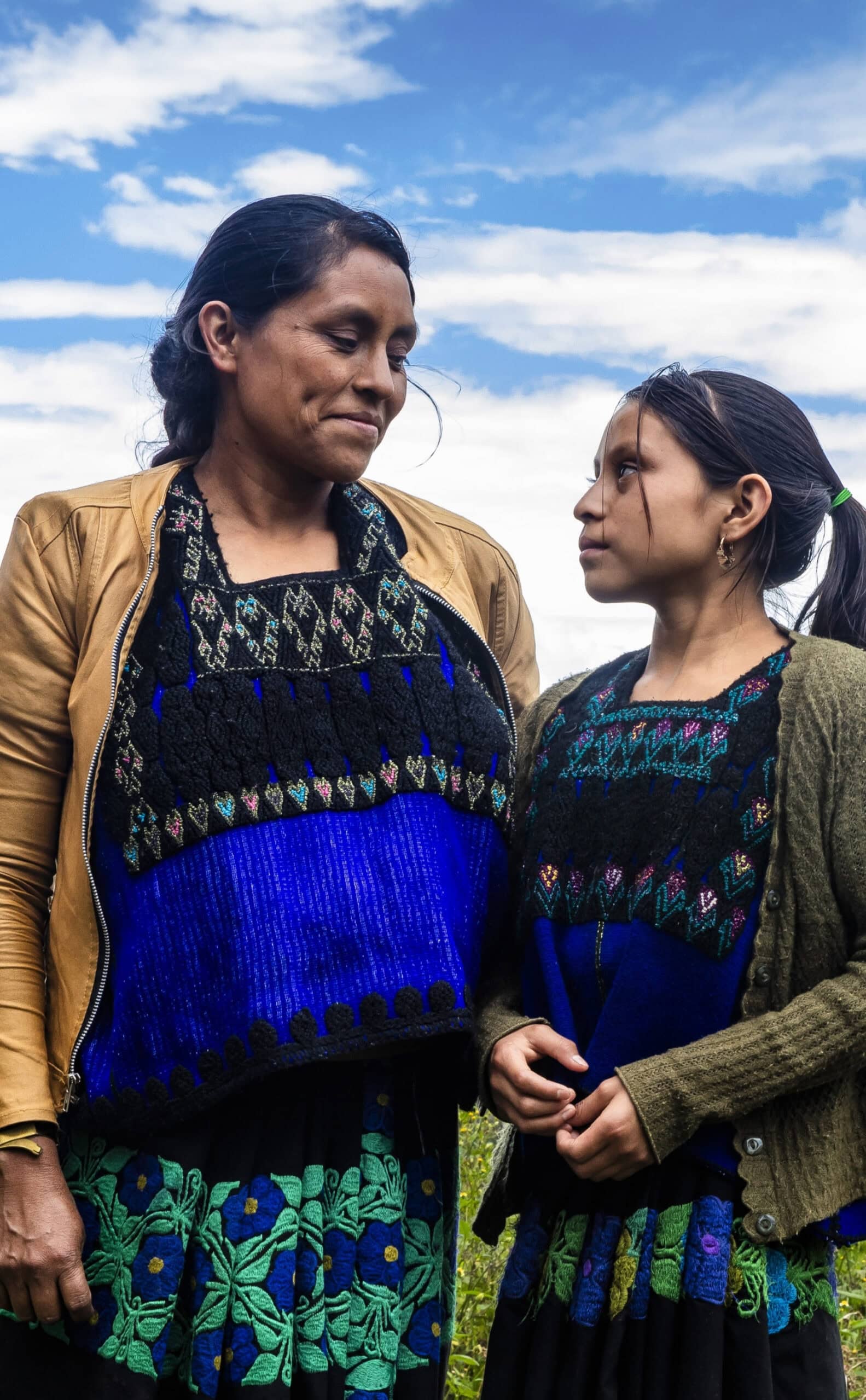 Mother and Daughter in Mexico Wearing Embroidered Dress Mother and daughter in Mexico, standing together outdoors under a blue sky.