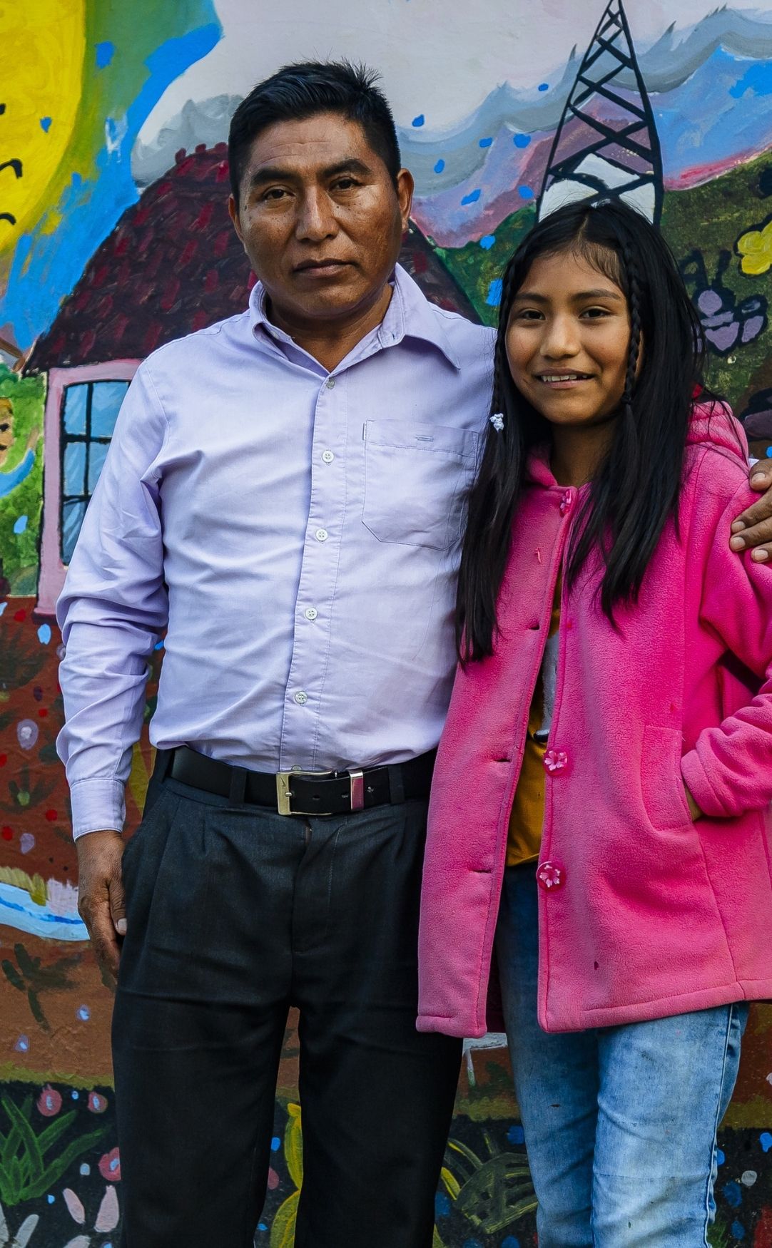Father and Daughter Standing Together in Mexico Community Portrait A father and young girl standing together in front of a colorful mural in Mexico, smiling and posing for a community portrait.