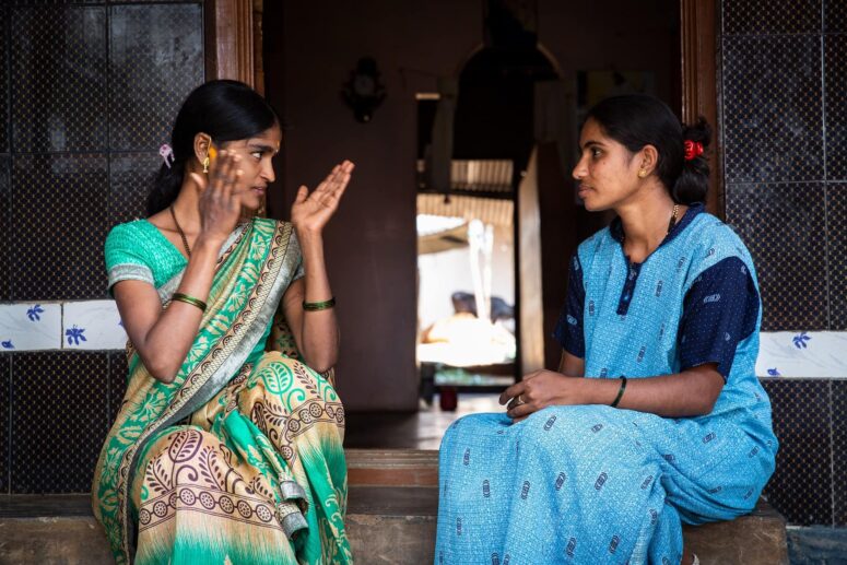 Two young women sitting with traditional India clothing. They are talking and looking at each other.